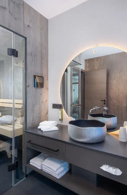 Modernes Badezimmer mit großem, rundem Spiegel und angrenzender Sauna