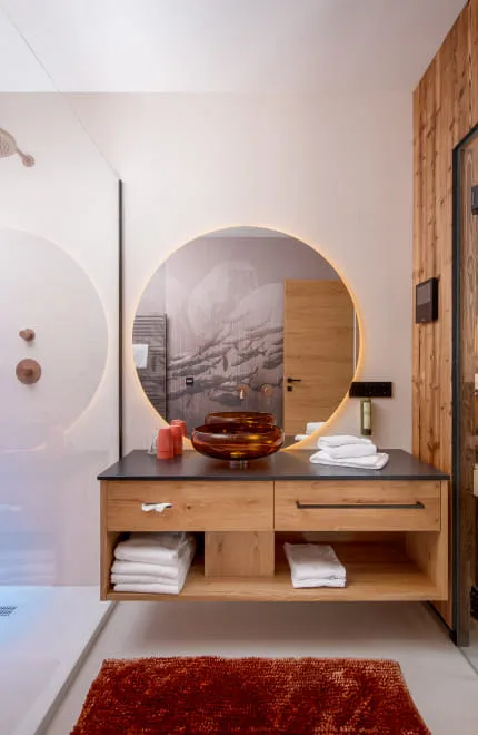 Modernes Badezimmer mit großem, rundem Spiegel und angrenzender Sauna