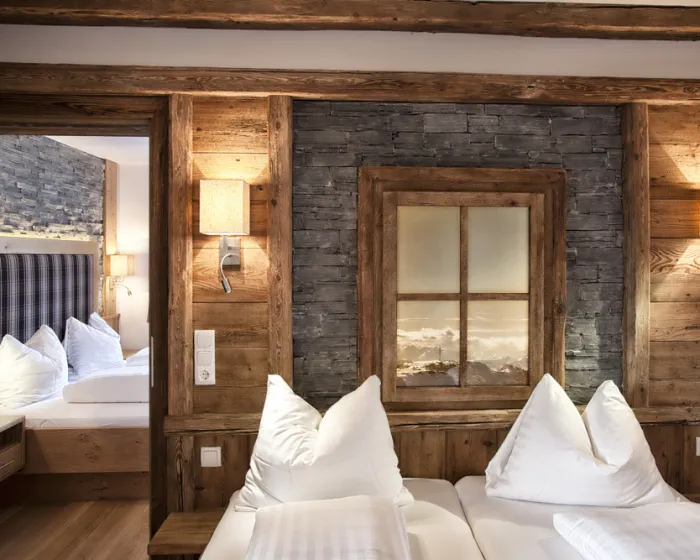 Nahaufnahme Doppelbett vor Holzwand mit angrenzendem weiterem Schlafzimmer